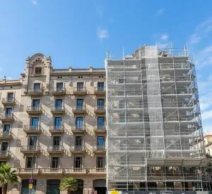 Fachada de edificio clásico en Barcelona con sistema de andamios y malla de seguridad para obras de restauración técnica.