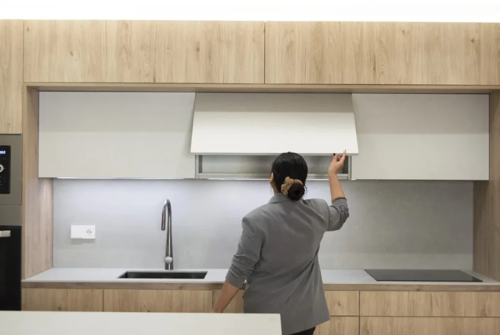 Mujer abriendo un armario superior en una cocina moderna con muebles de madera clara y encimera gris en proyecto Sicília