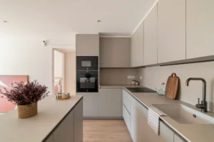 Cocina moderna con isla central en reforma integral de vivienda en Sant Andreu, Barcelona, featuring mobiliario blanco y encimera oscura.