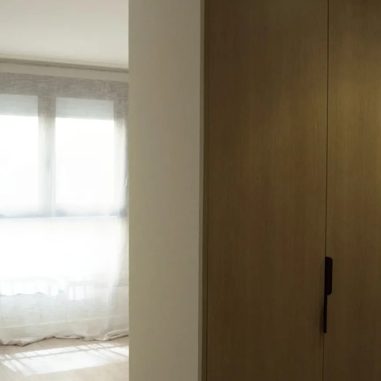Pasillo moderno con armario de madera clara y entrada a habitación luminosa con cortinas blancas en proyecto Sicília
