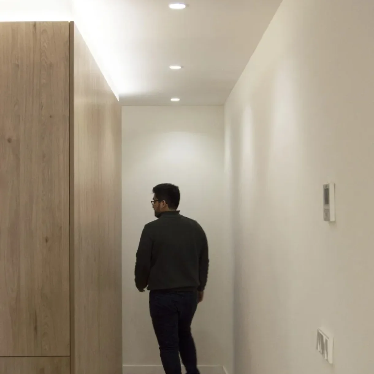 Hombre caminando por un pasillo moderno con iluminación LED empotrada y armario de madera en el proyecto Sicília