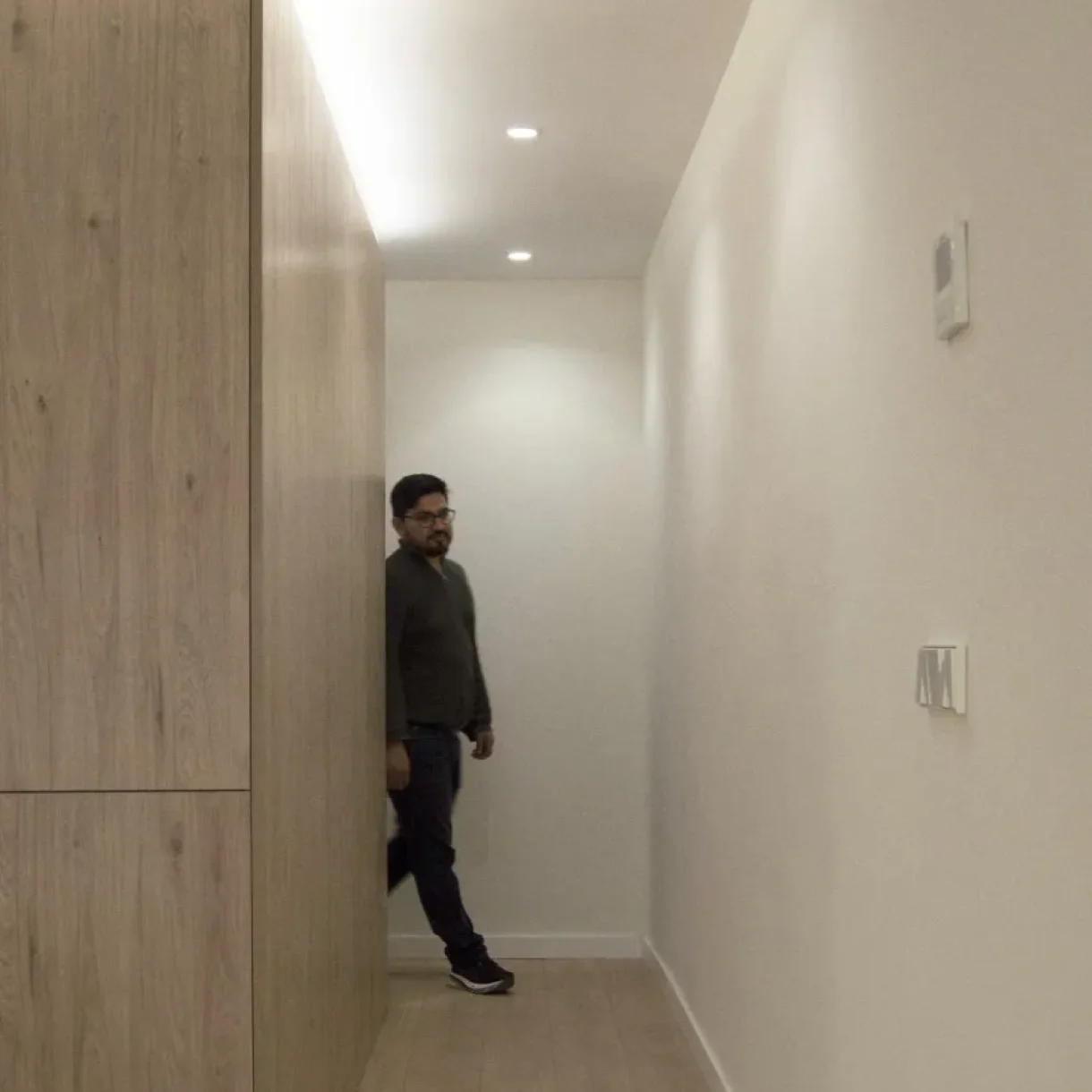 Hombre en pasillo moderno con armarios de madera clara y luces empotradas, proyecto Sicília Barcelona