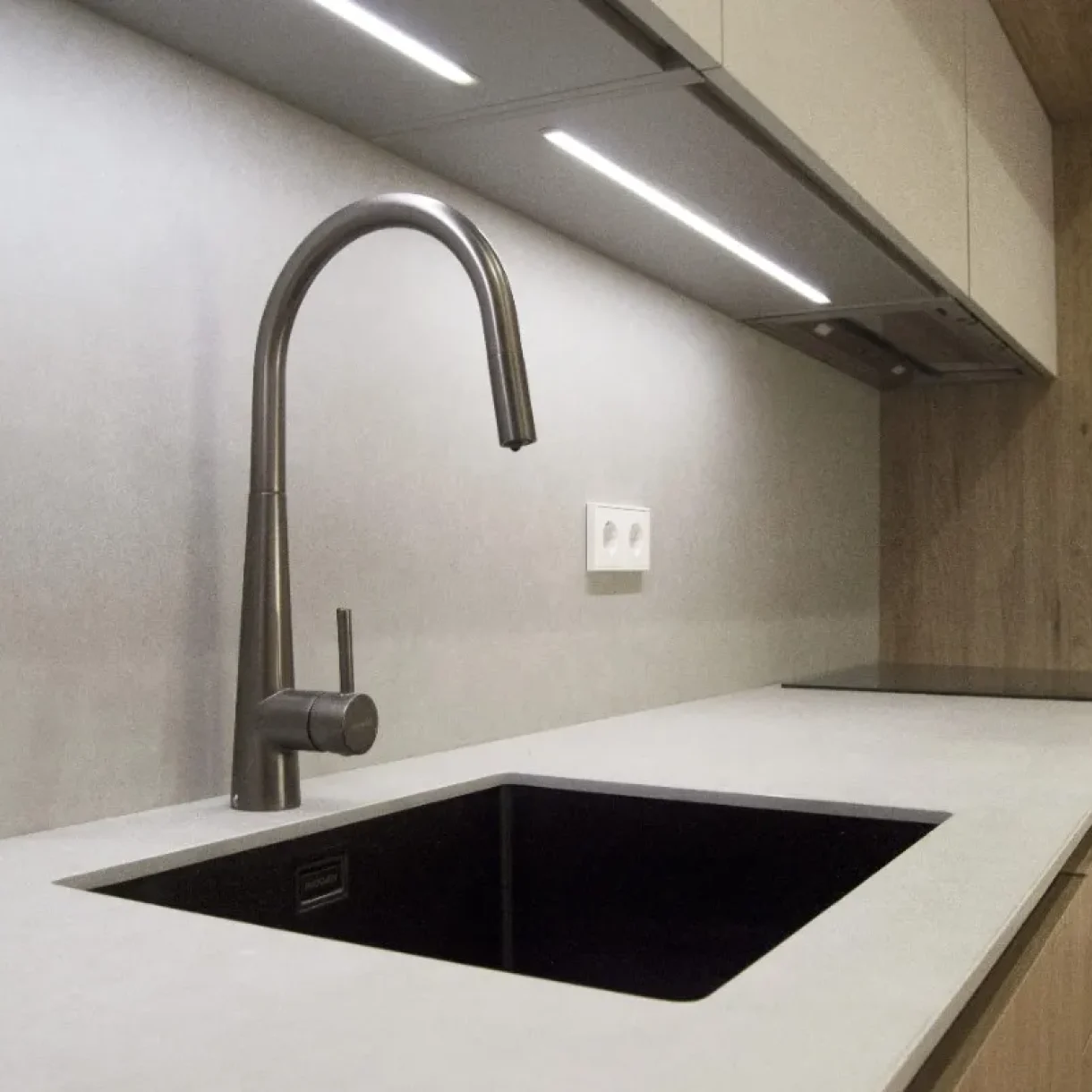 Cocina moderna en proyecto Sicília, Barcelona, con grifo negro, fregadero bajo encimera y luces LED bajo gabinetes.
