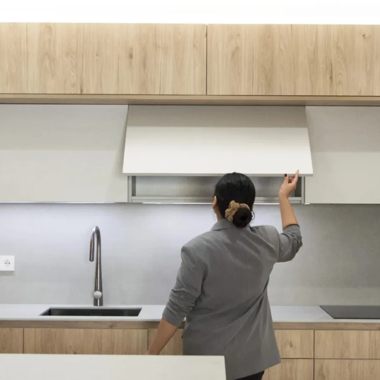 Mujer abriendo un armario superior en una cocina moderna con muebles de madera clara y encimera gris en proyecto Sicília
