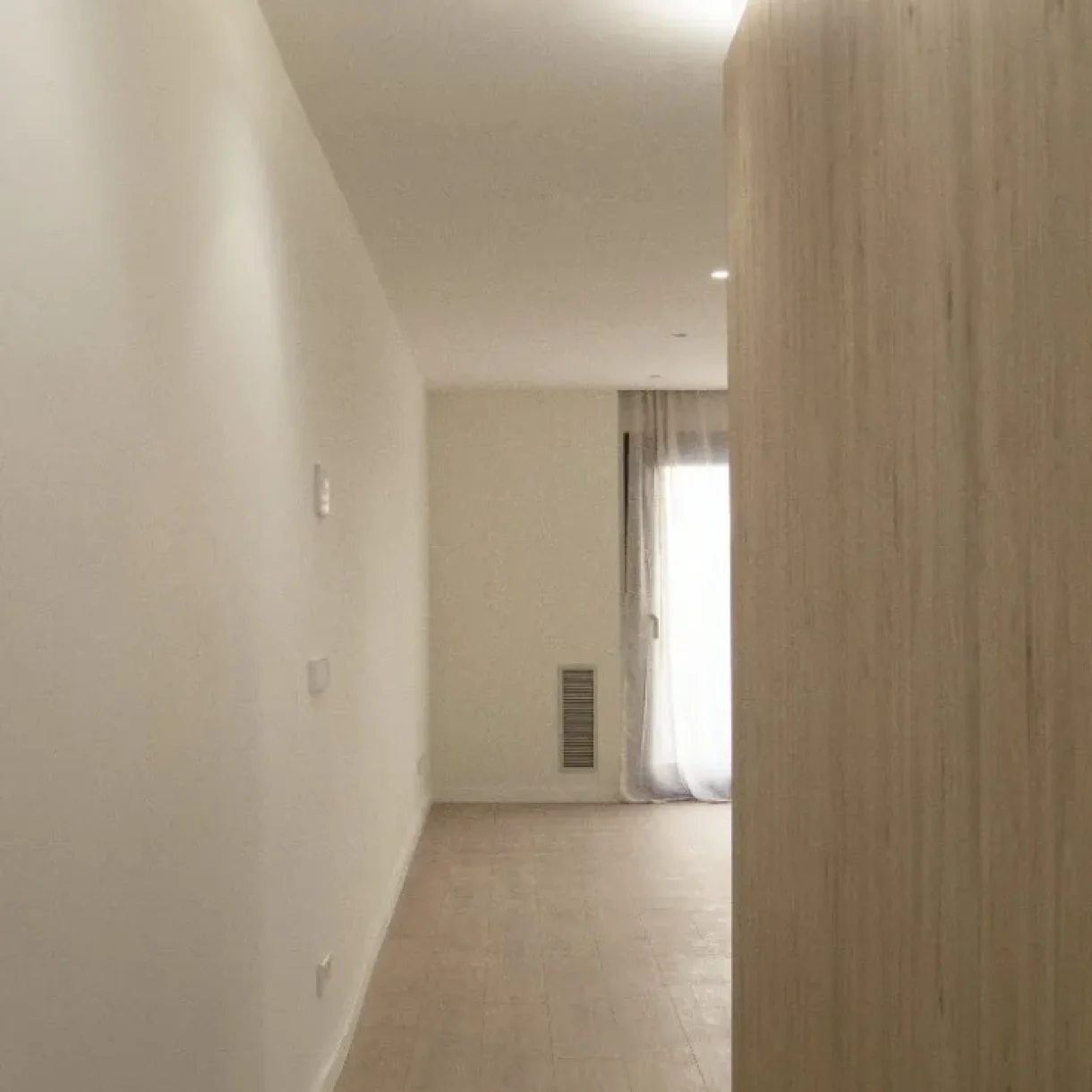 Pasillo moderno y luminoso en proyecto de vivienda en Sicília, Barcelona, con paredes blancas y suelo de madera clara