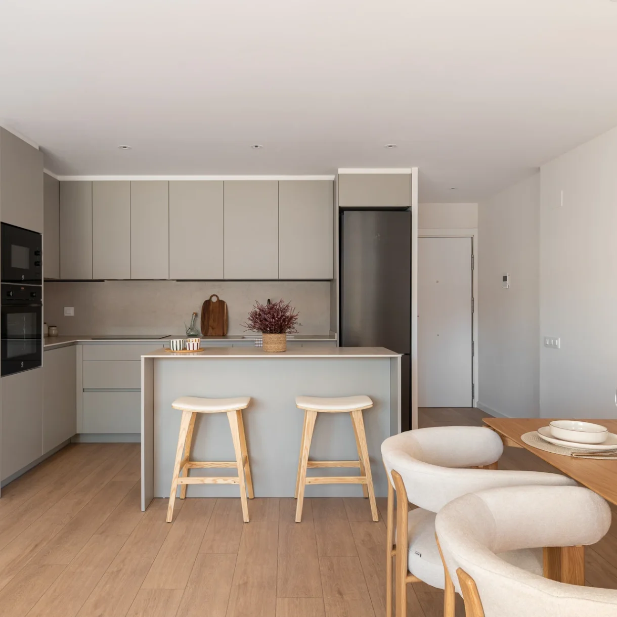 Diseño de cocina comedor moderna en Sant Andreu con isla central, acabados en madera clara y detalles en negro, maximizando la luz natural.