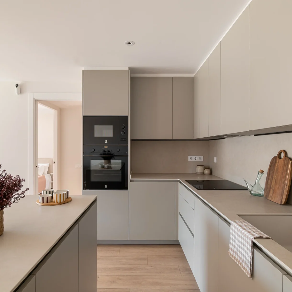 Cocina moderna con isla central en reforma integral de vivienda en Sant Andreu, Barcelona, featuring mobiliario blanco y encimera oscura.