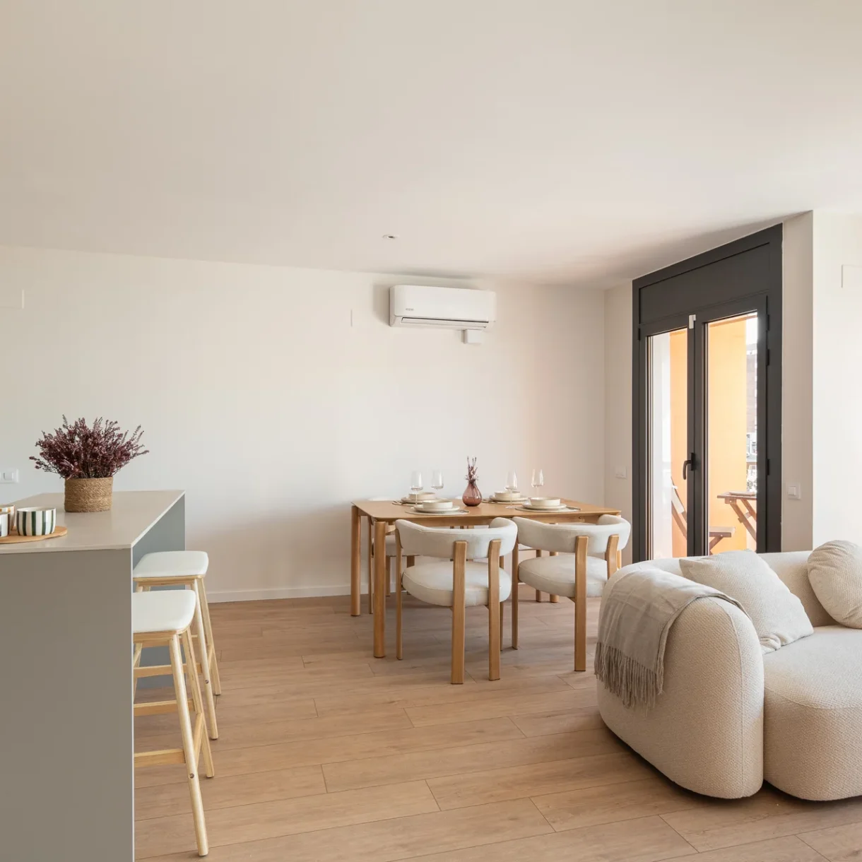 Salón-comedor moderno y luminoso en Sant Andreu, Barcelona, con sofá gris, mesa de centro de madera, y estanterías integradas, reformado por interioristas.