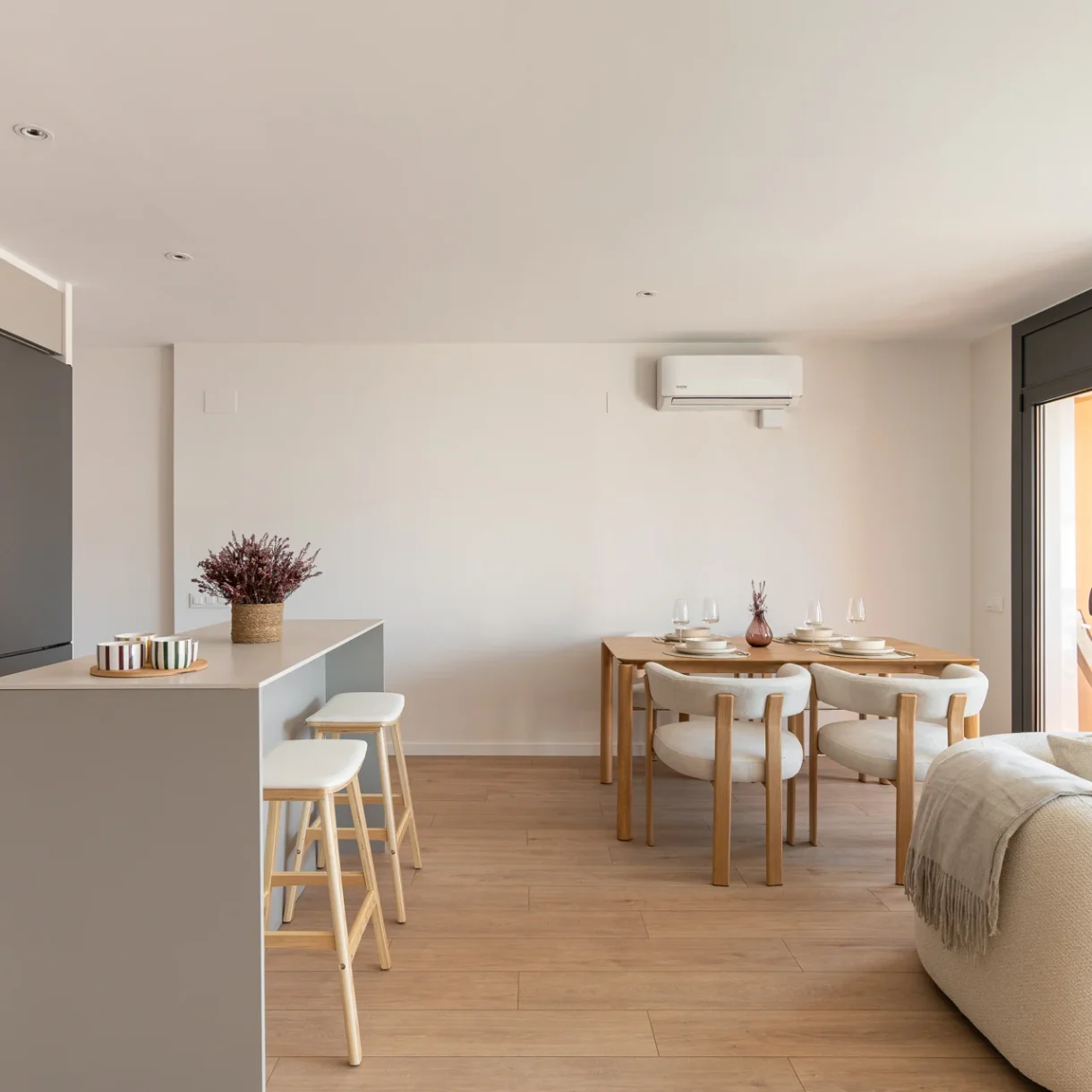 Vista detallada de una cocina con isla abierta al salón, mostrando la barra americana de madera y la moderna campana extractora sobre la placa de inducción en una reforma de piso en Sant Andreu.